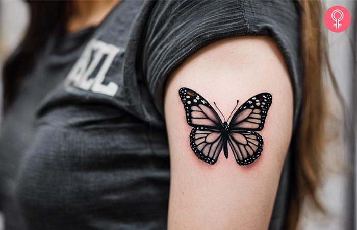 A black and white monarch butterfly tattoo on a woman’s upper arm