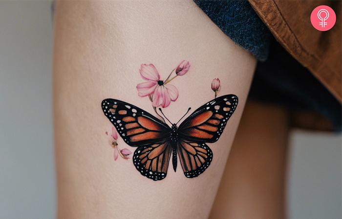 A monarch butterfly tattoo with flowers on a woman’s thigh