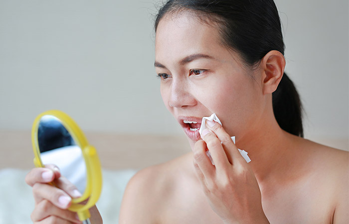 Woman looks into handheld mirror as she wipes lipstick off to proceed with lipcare