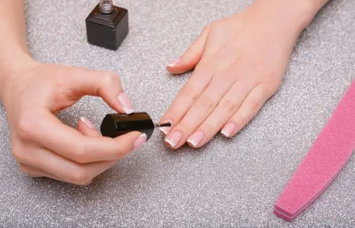 A woman applying a top coat to her nails