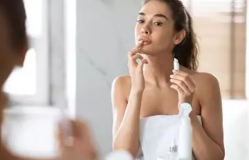 A woman applying lip balm to moisturize her lips