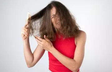Woman having trouble combing her dull hair that has tangled due to split ends