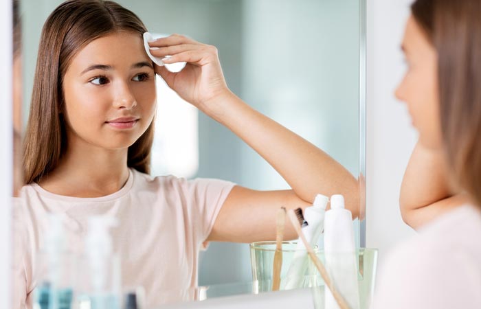 Teenage girl looking into the mirror and cleaning her face with cotton cleansing pad