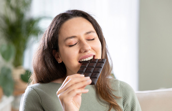 Woman eating a bar of dark chocolate to improve blood flow to her skin and get a youthful glow