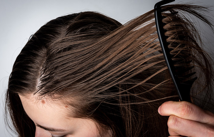 Closeup of woman combing hair that is oily from excess sebum production due to hormonal imbalance