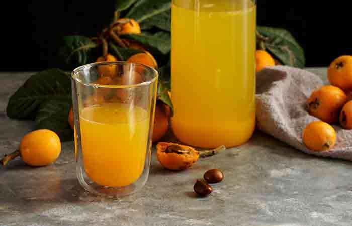 A glass and beaker of fresh loquat juice against a background of loquat fruits