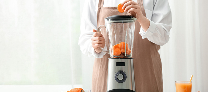 Woman putting chopped carrots to a blender