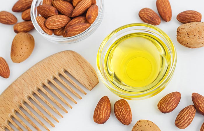 Overhead view of a spread of almonds and a bowl of almond oil beside a wooden comb