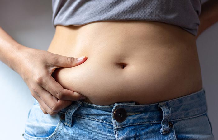Woman pinches her bloated stomach as a side effect of eating too many almonds