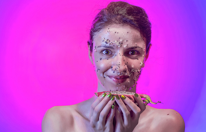 Woman with dragon fruit mask on face poses with half a slice of the fruit