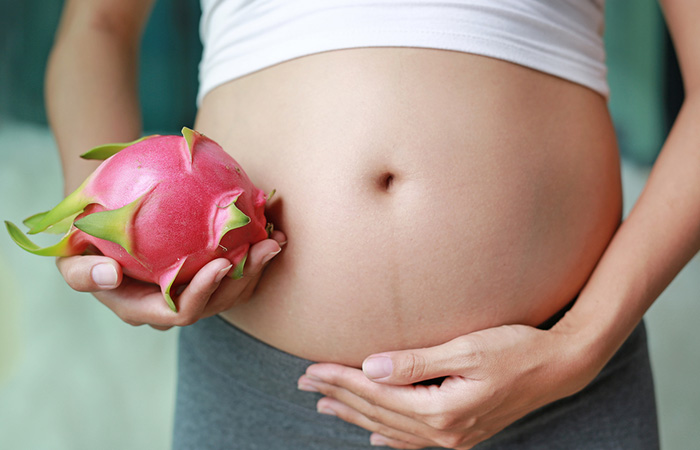 Pregnant woman holds a whole dragon fruit beside her belly