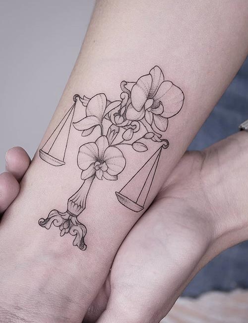 Libra tattoo represnted by scales and adorned with flowers