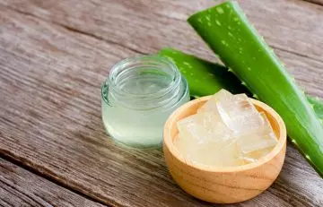 A container and bowl of aloe gel beside sliced aloe vera