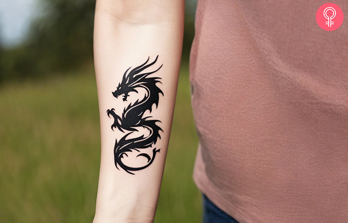 A woman with a minimalist black dragon tattoo on her forearm.