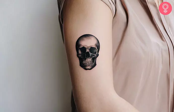 A woman showing a small black skull tattoo on her arm