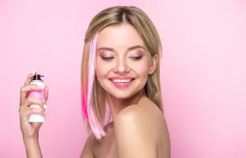 A girl sprays dry shampoo on her dyed hair