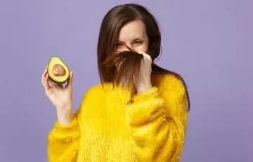 Woman holding an avocado as she's happy with its hair benefits.