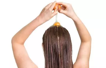 Woman applying egg to condition her dry hair