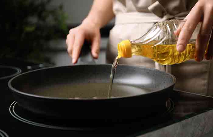 Close up of a chef pouring sunflower oil onto a pan on the stove