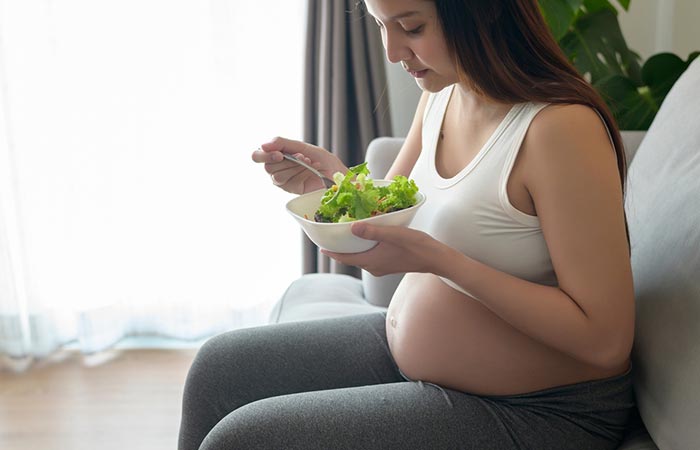 Pregnant woman having fresh lettuce salad at home.