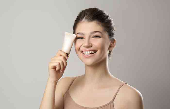 Woman holding a tube of tinted moisturizer beside her face