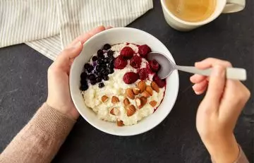 Woman eating a bowl of oats topped with black currants and other berries