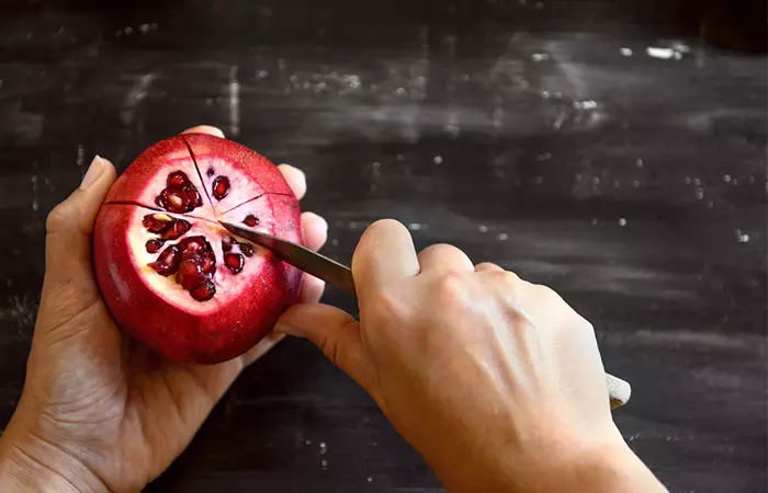 Close-up of hands cutting and peeling a pomegranate.