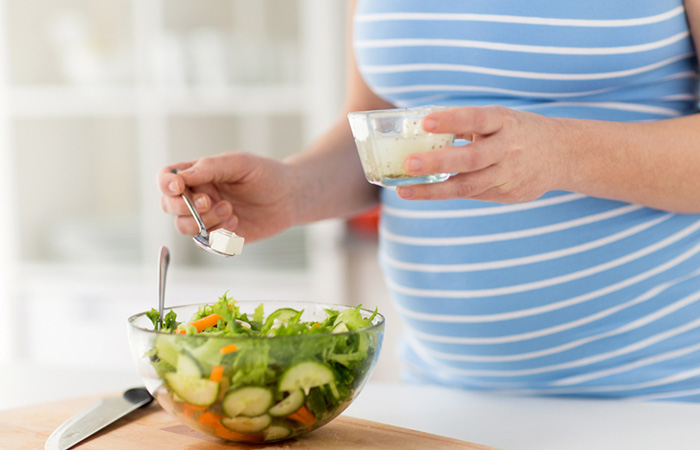 Pregnant woman adding cheese to her salad