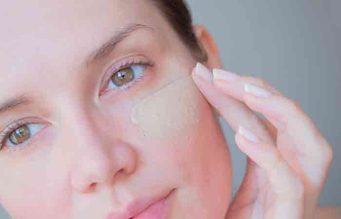 Woman applying tinted moisturizer on her cheeks