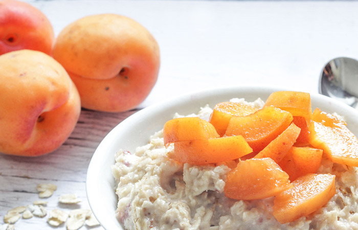 A bowl of oatmeal topped with apricot slices with whole apricots in the background