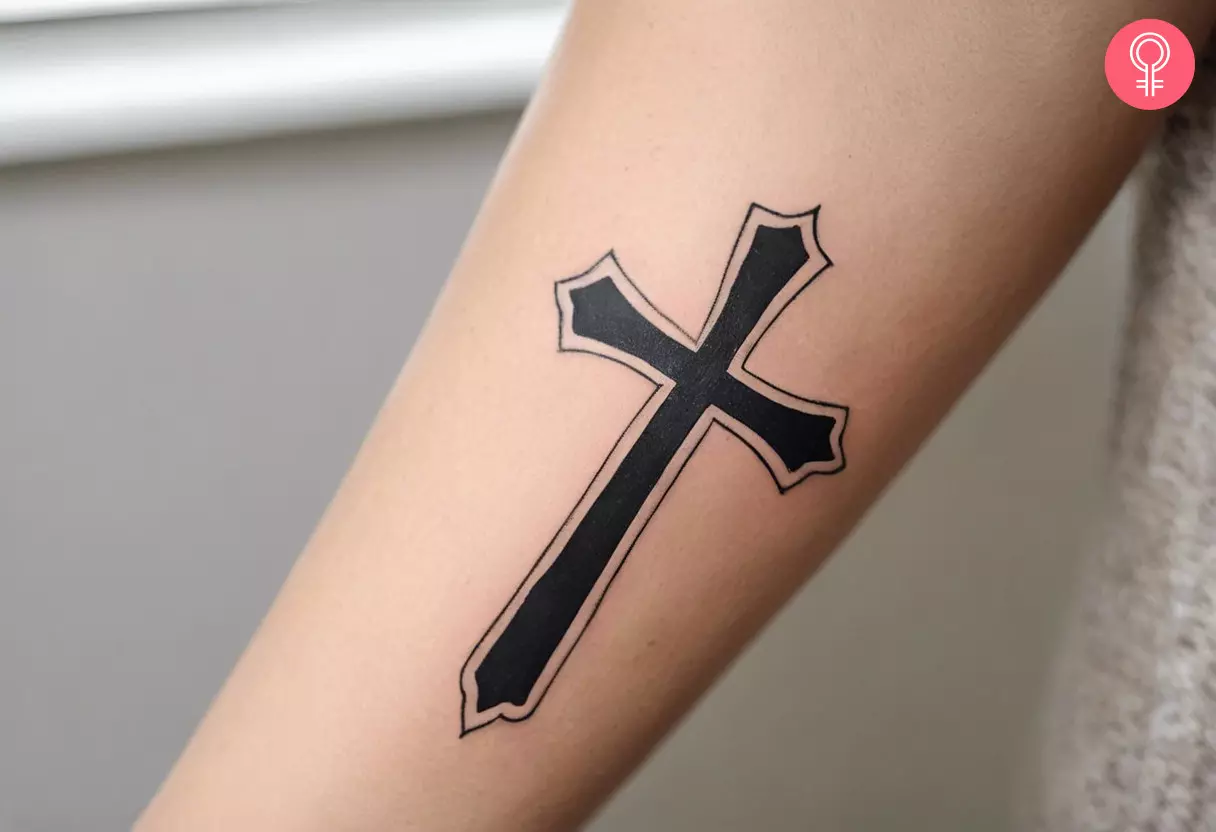 A cross tattoo design on the forearm of a woman