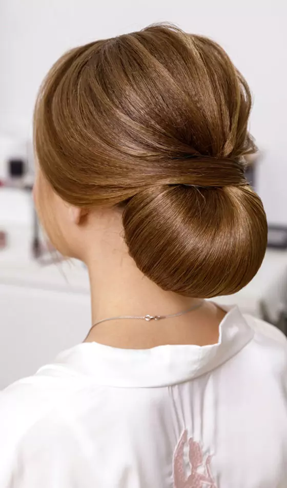 A woman with shiny hair sporting a low bun hairstyle