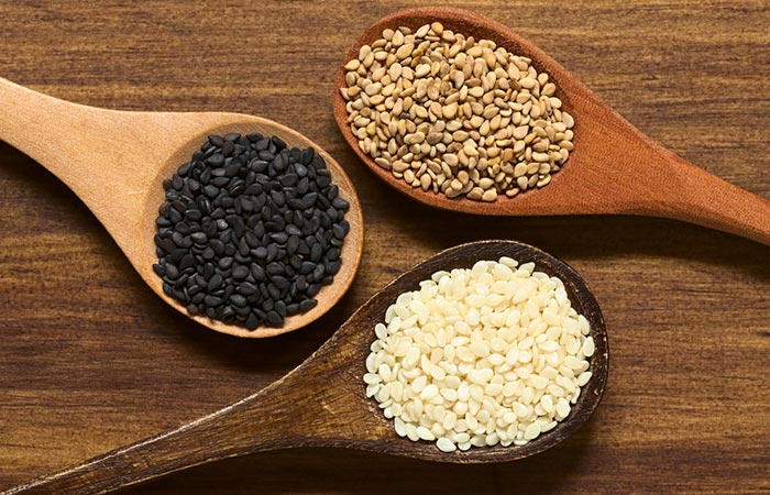 Close up of black, white and roasted sesame seeds on wooden spoons.