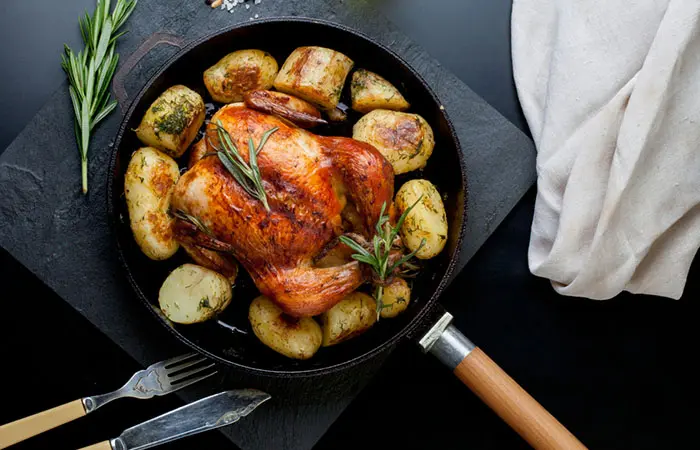 A full baked chicken, with a side of baked potatoes, with rosemary garnish