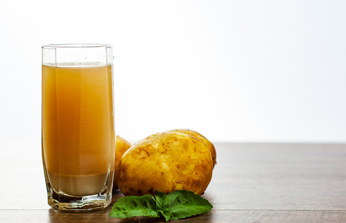 A glass of potato juice beside some potatoes