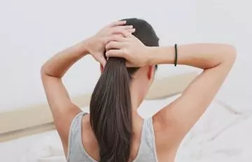 Woman loosely tying her hair with oil to prevent sweating-related hair loss