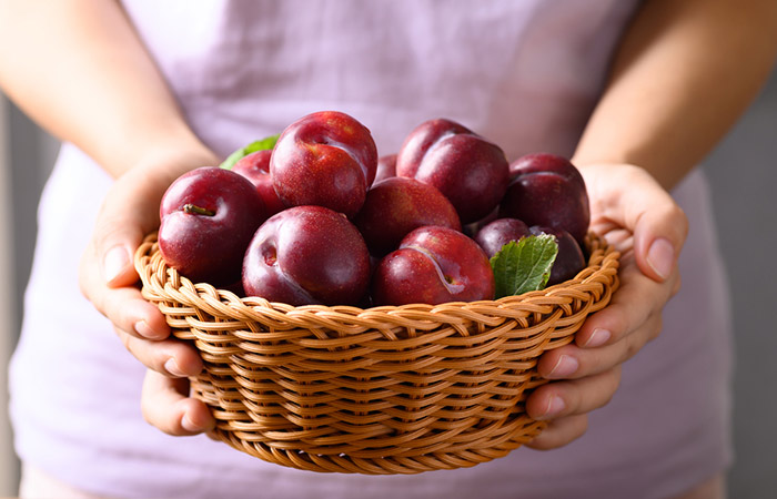 Woman holding a basket full of plums