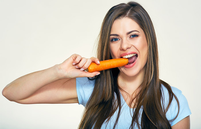 Frau mit gesundem Haar, die glücklich eine Karotte beißt