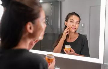 Woman looking into a mirror while applying honey mask on the face