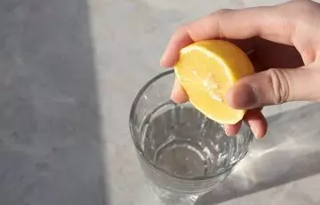 Hand squeezing lemon juice in a glass of water