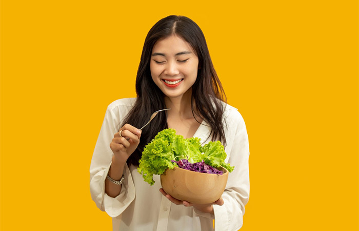 Woman eating cabbage and lettuce salad for Vitamin K. 