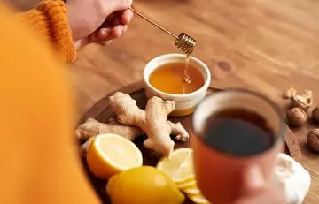 Woman adding honey to a warm cup of ginger tea