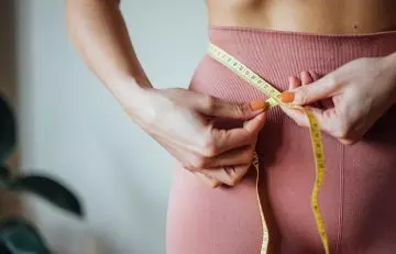 Woman measuring her waist to depict weight loss