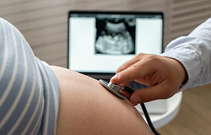 Doctor using stethoscope on tummy of pregnant woman for a prenatal check up after an ultrasound scan
