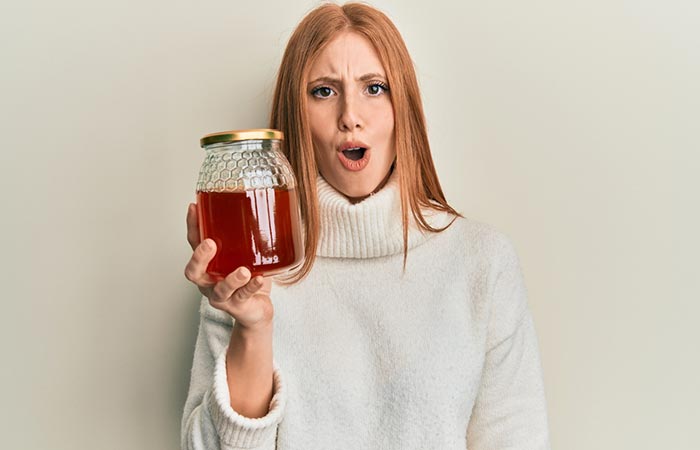 Woman holding a jar of honey surprised at its side effects