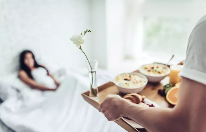 A young woman is in bed as her spouse brings scrumptious comfort food.