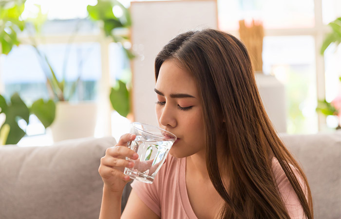 Young Asian woman drinking water while sitting on sofa at home.