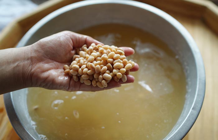 Person scoops a handful of soaked soybeans out of the bowl.