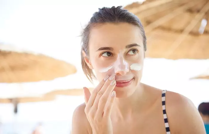 Woman applying sunscreen to her face to prevent aging