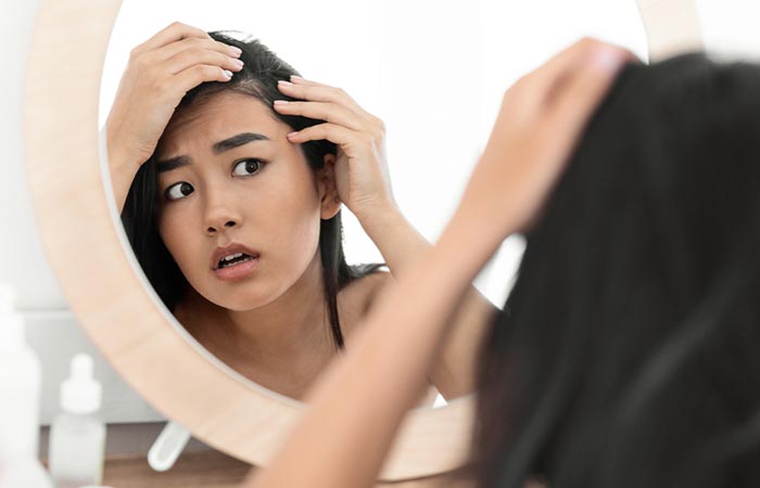 A worried woman looking at her thinning hairline in the mirror 